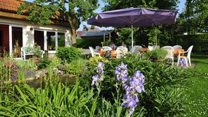 An outdoor seating area with white chairs and a purple umbrella, surrounded by lush greenery and flowers. - Gasthaus Zum Rethberg (Lübstorf)