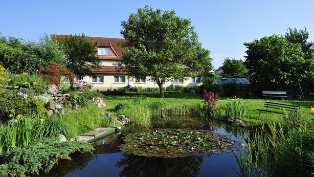 A house with a garden, pond, and a bench. - Gasthaus Zum Rethberg (Lübstorf)