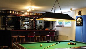 A pool table with a cue stick, a dartboard, and a bar area with stools and shelves. - Gasthaus Zum Rethberg (Lübstorf)