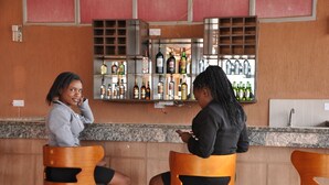 Deux personnes sont assises au bar, avec une variété de bouteilles et de verres disposés derrière elles.