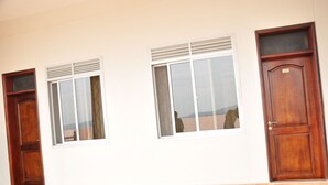 Une pièce dotée de trois portes en bois, de deux fenêtres équipées de stores et d’un sol carrelé.