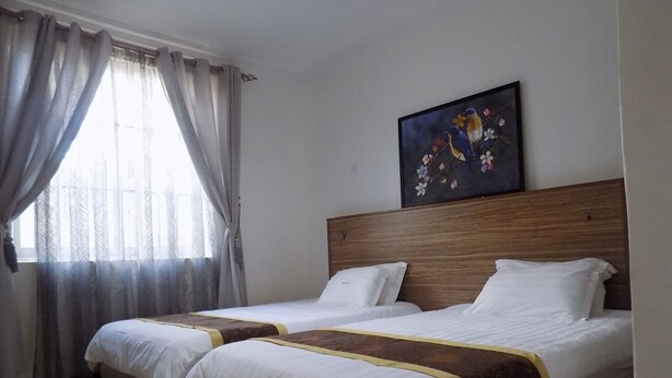 A hotel room with two beds, a wooden headboard, a painting of birds, and a window with curtains. - Remmings Hotel (Kampala)
