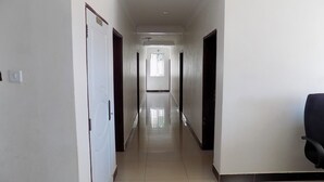 A long, narrow hallway with white walls and a tiled floor, leading to a bright room with a window. - Remmings Hotel (Kampala)