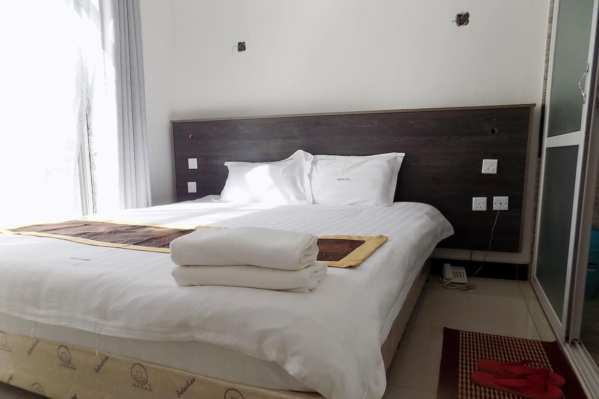 A hotel room with a bed, a bedside table, a telephone, and a window.