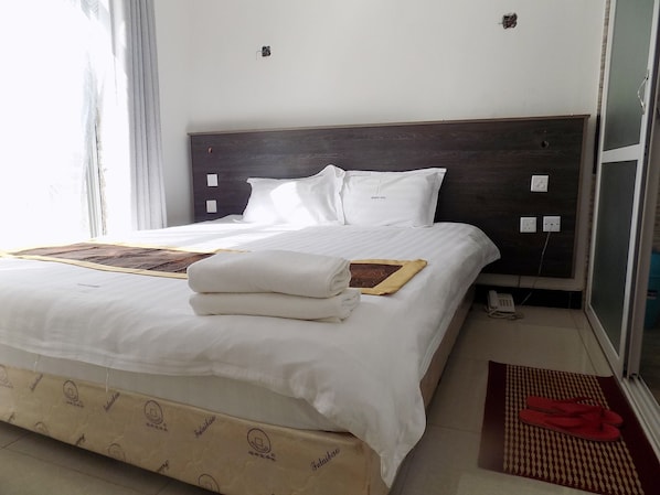 A hotel room with a bed, a bedside table, a nightstand, a window, and a door.