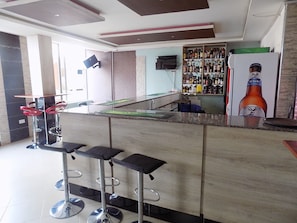A bar area with a counter, stools, a television, and a shelf with bottles.