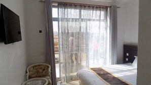 A hotel room with a bed, a chair, a small table, and a TV on the wall. - Remmings Hotel (Kampala)