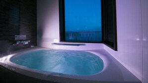 A modern bathroom with a large bathtub, a window with a view, and a shower area. - Ofunato Onsen (Ofunato)