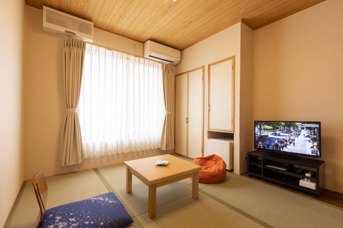 Quarto com piso de tatame, televisão, mesa de madeira, um pufe e uma porta deslizante.