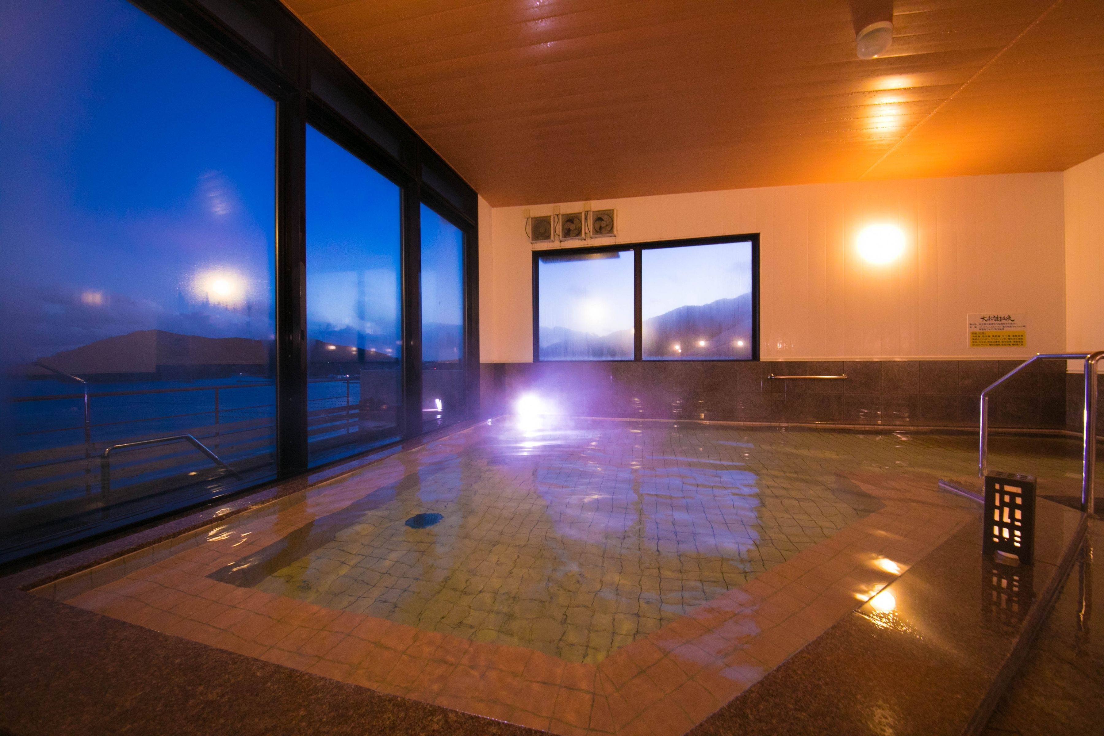 An indoor swimming pool with large windows, a tiled floor, and a view of the mountains.