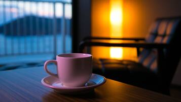 A pink cup on a saucer on a wooden table with a view of a balcony and a lit lamp in the background.