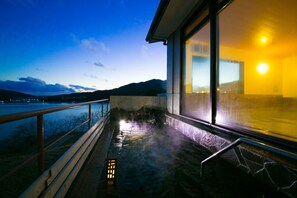 Zona de aguas termales con vistas a las montañas y un cuerpo de agua al atardecer.
