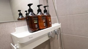 Un baño con un lavamanos blanco, tres botellas de jabón corporal y un cabezal de ducha.