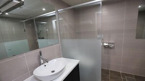 Un baño moderno con un lavamanos blanco, un espejo y una zona de ducha.