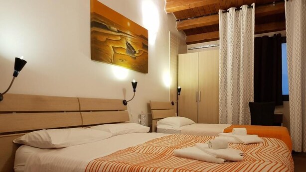 A hotel room with two beds, a wooden headboard, a painting on the wall, and a wardrobe. - Terra del Sole B&B (Vittoria)