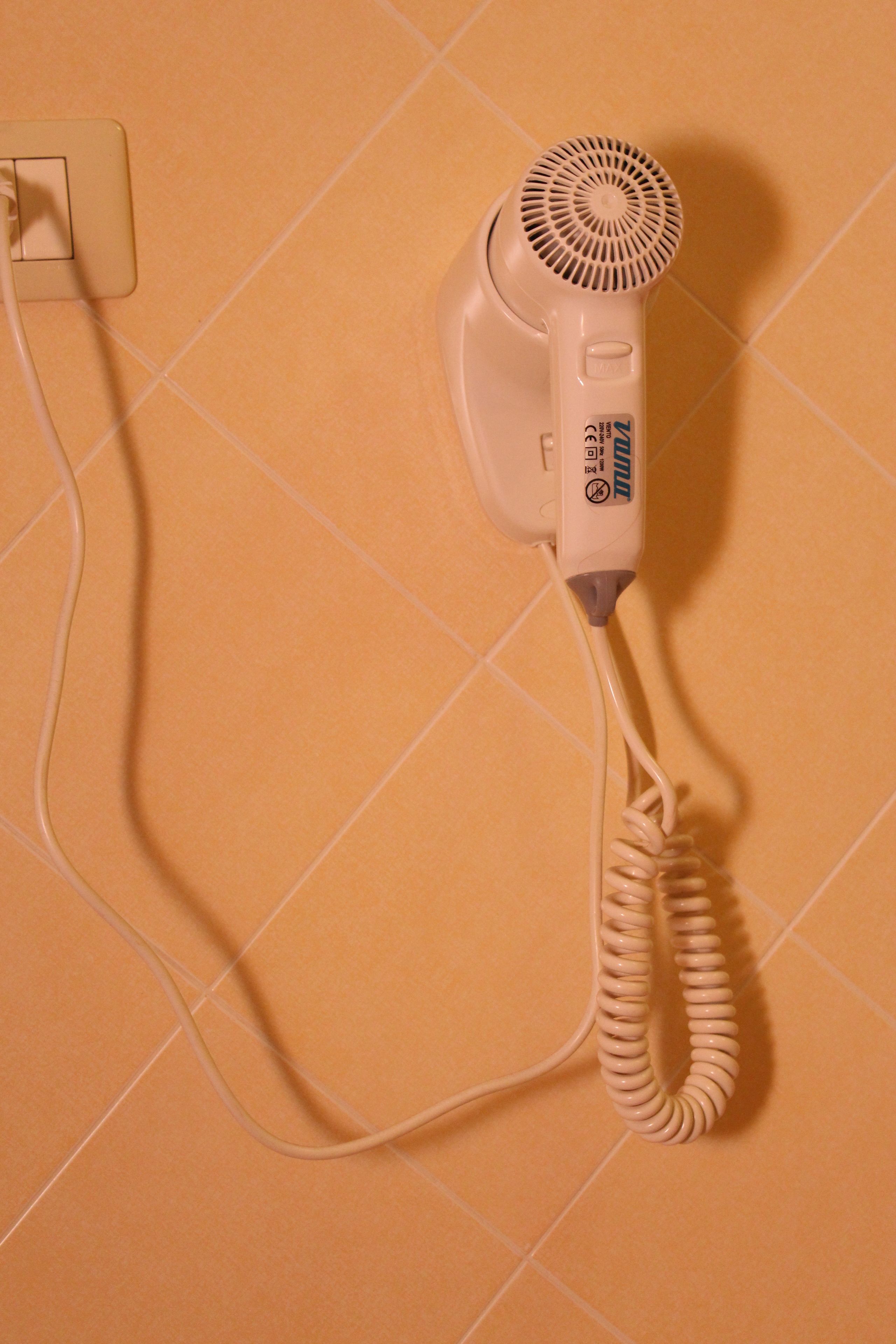 A hair dryer plugged into a wall socket on a tiled wall.