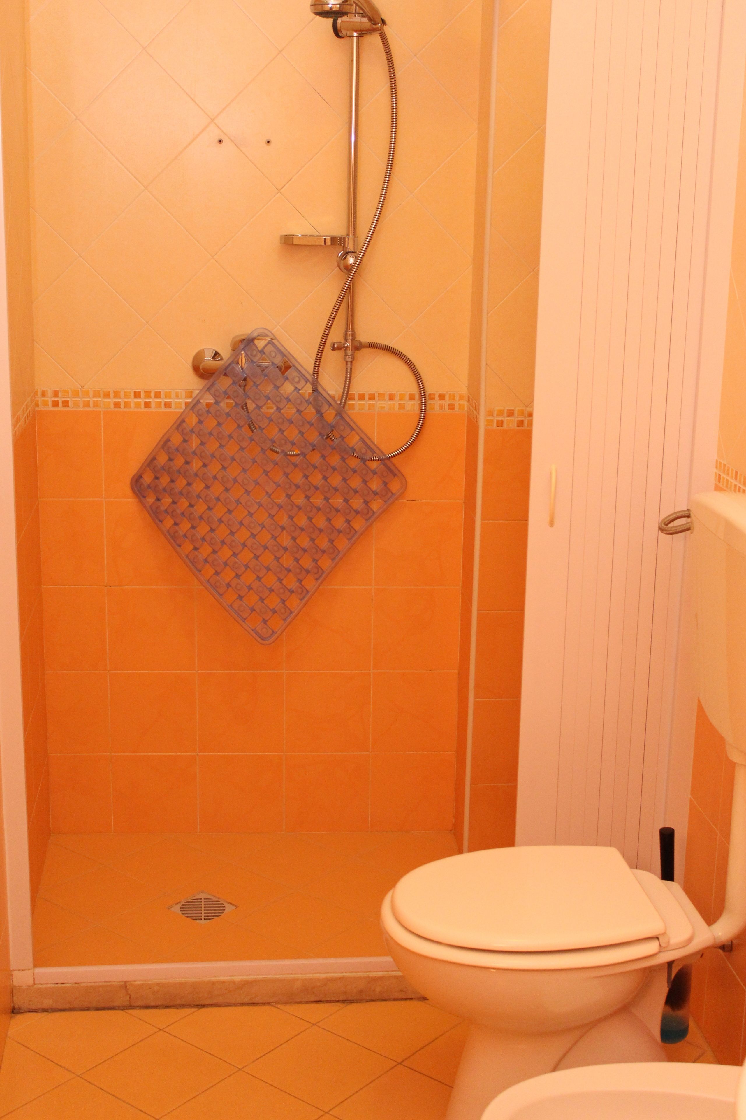 A bathroom with an orange tiled shower enclosure, a white toilet, and a visible shower hose.