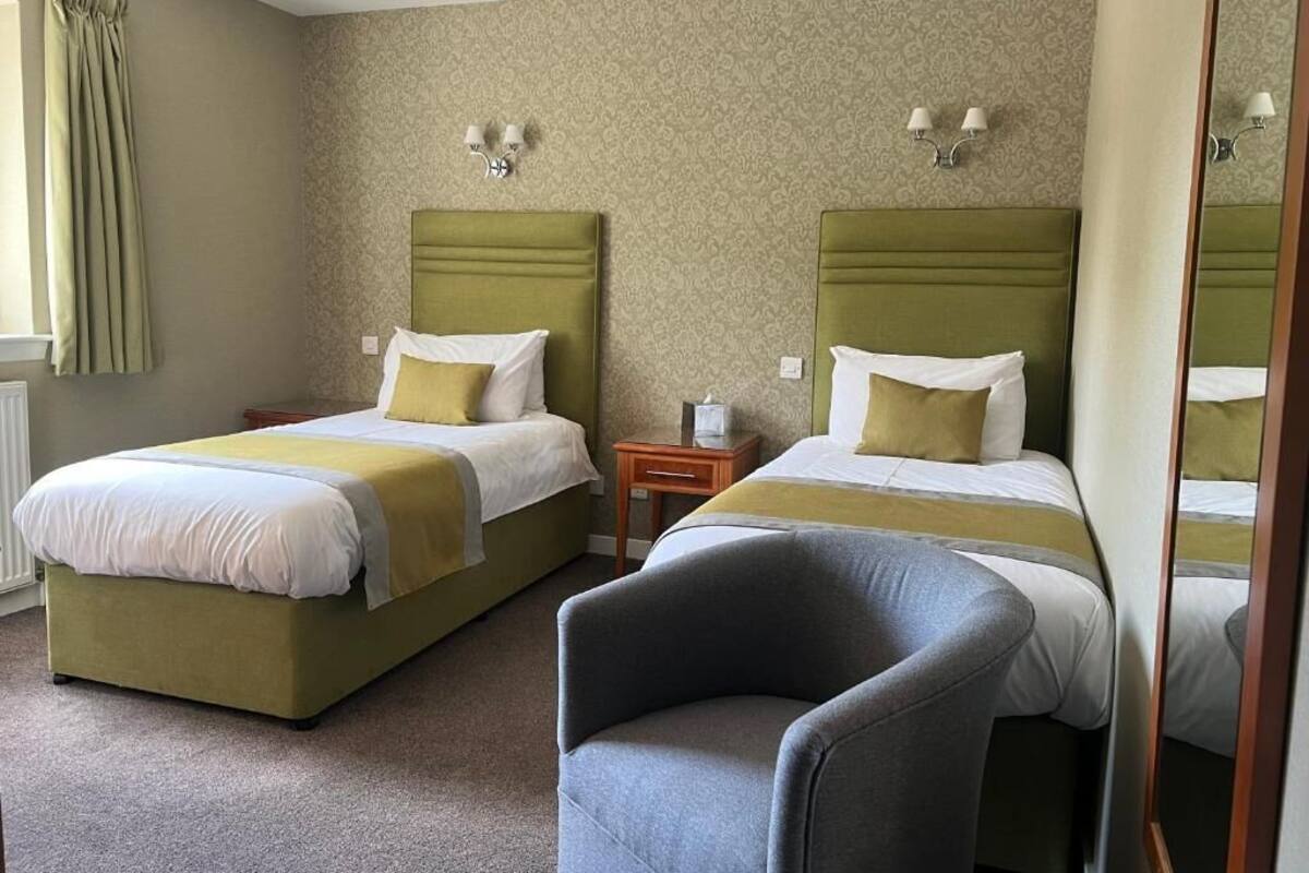 A hotel room with two beds, each with a headboard and pillows, a small wooden nightstand, a chair, and a mirror.