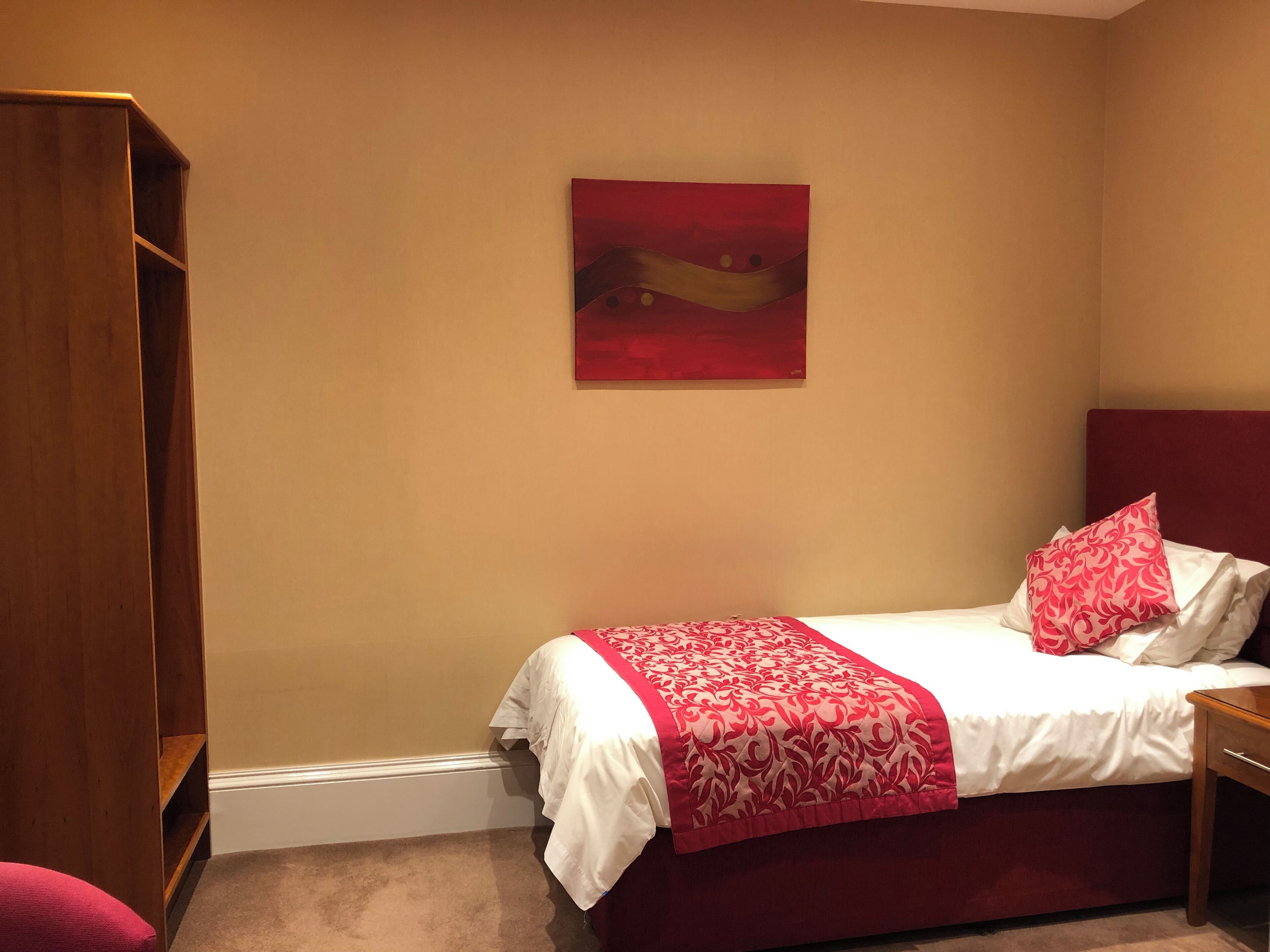 Un dormitorio con una cama, un armario de madera y un cuadro abstracto rojo en la pared.