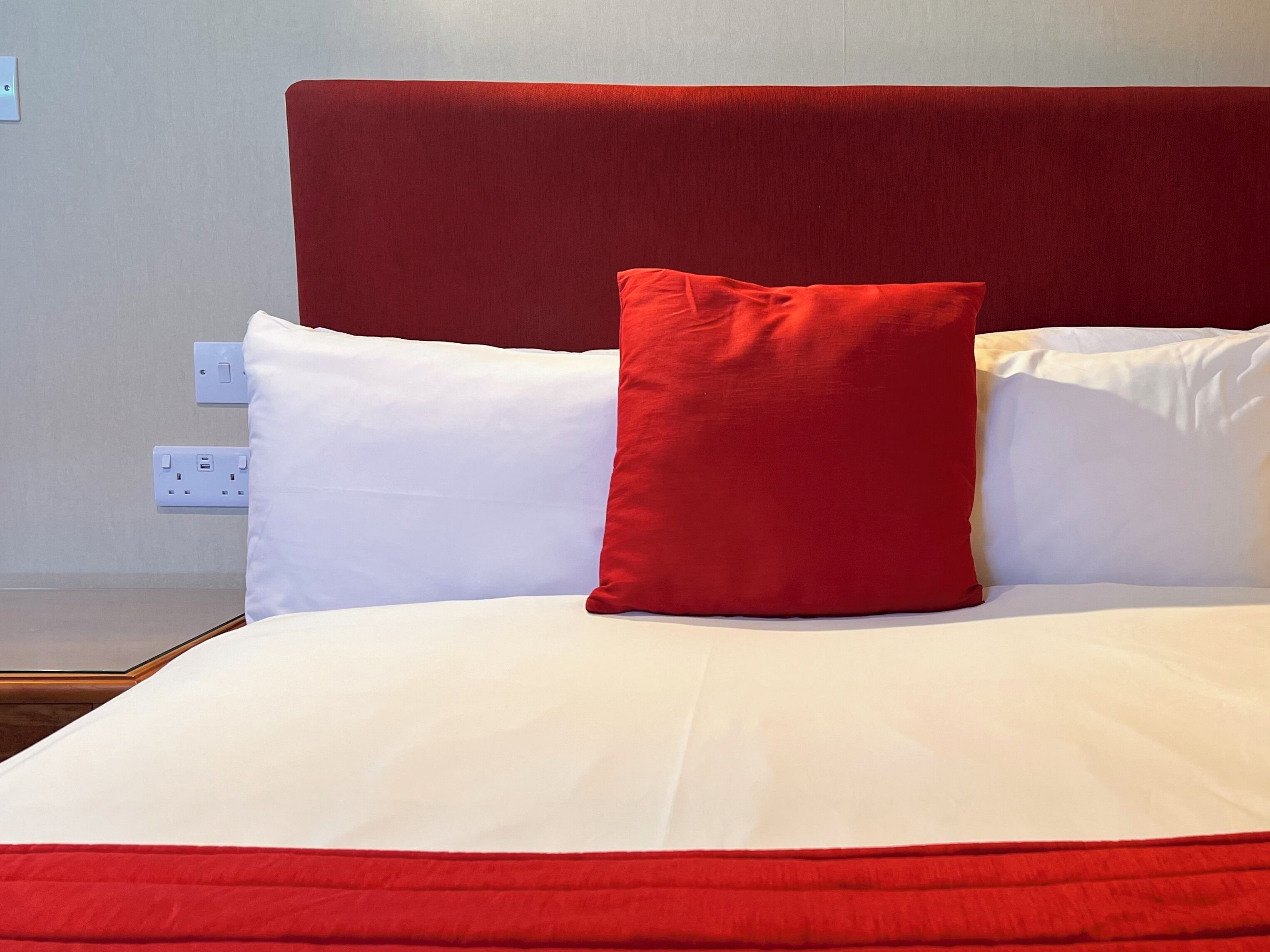 Una cama con cabecera roja, almohadas blancas y un cojín decorativo rojo.