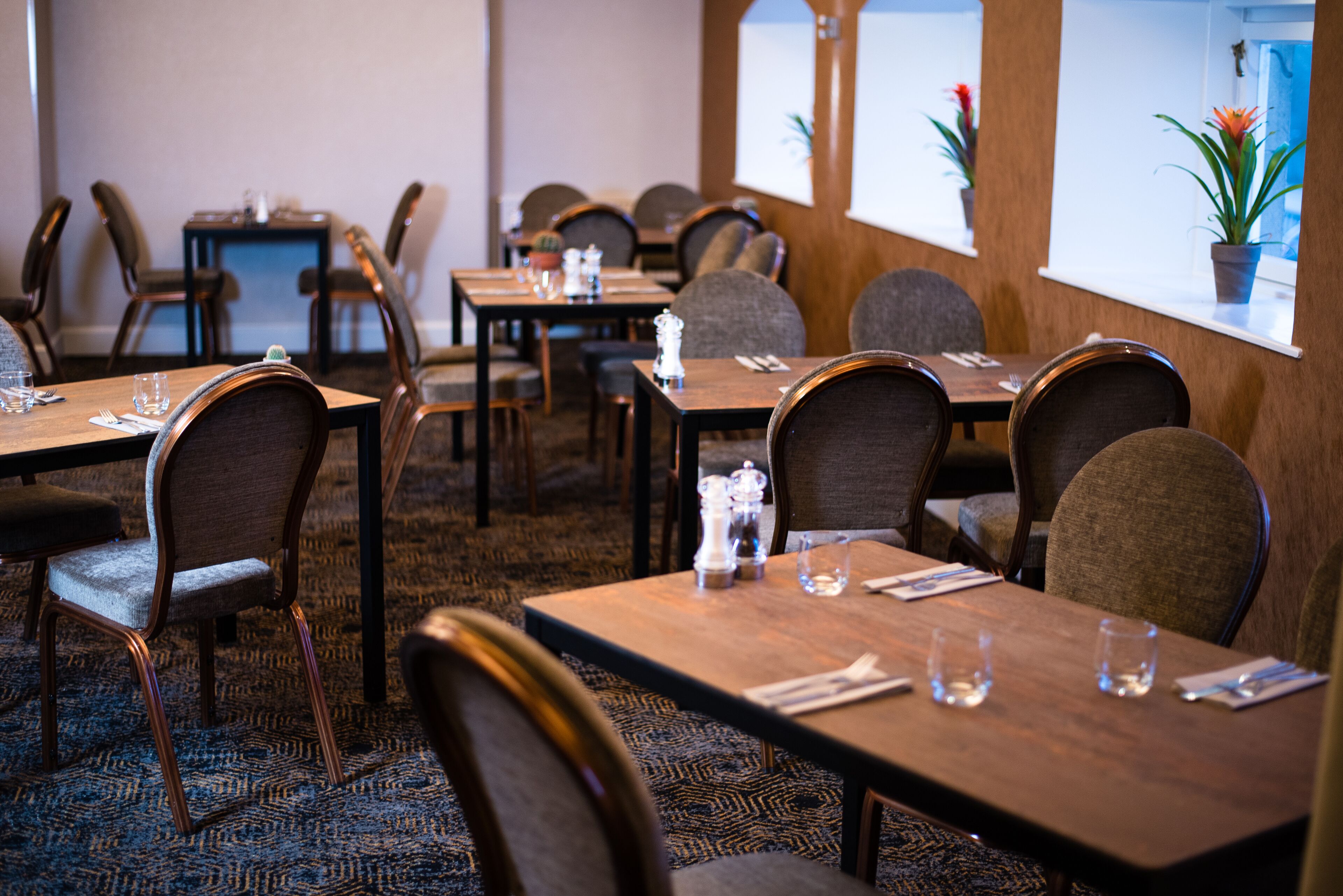 Un restaurante con varias mesas y sillas, cada conjunto con cubiertos y vasos.