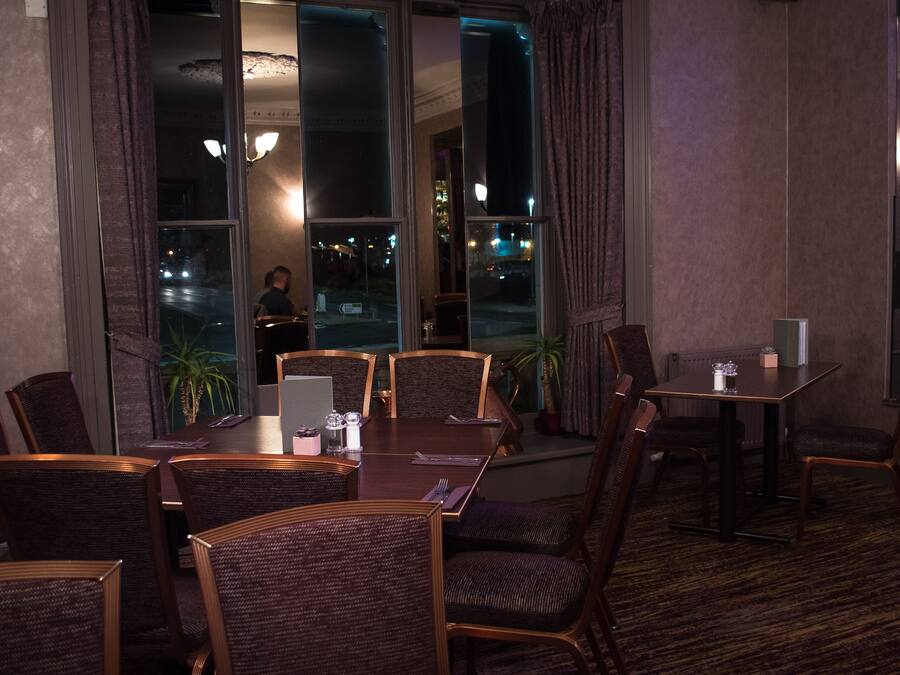 A dining area with a large table and chairs, a smaller table with a chair, and a view of the street outside.
