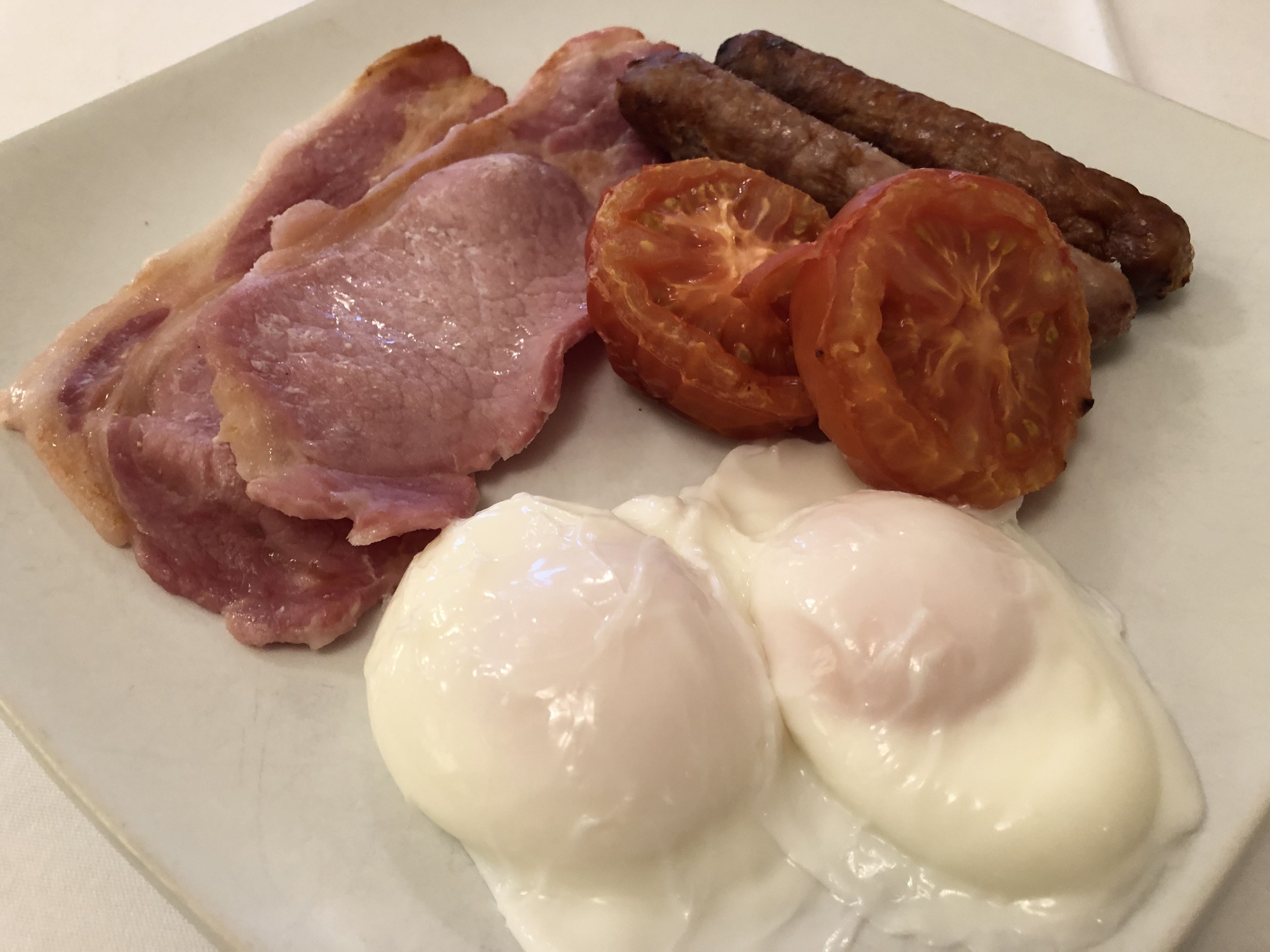 A plate with bacon, sausages, tomatoes, and poached eggs.
