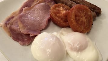 A plate with bacon, sausages, tomatoes, and poached eggs.