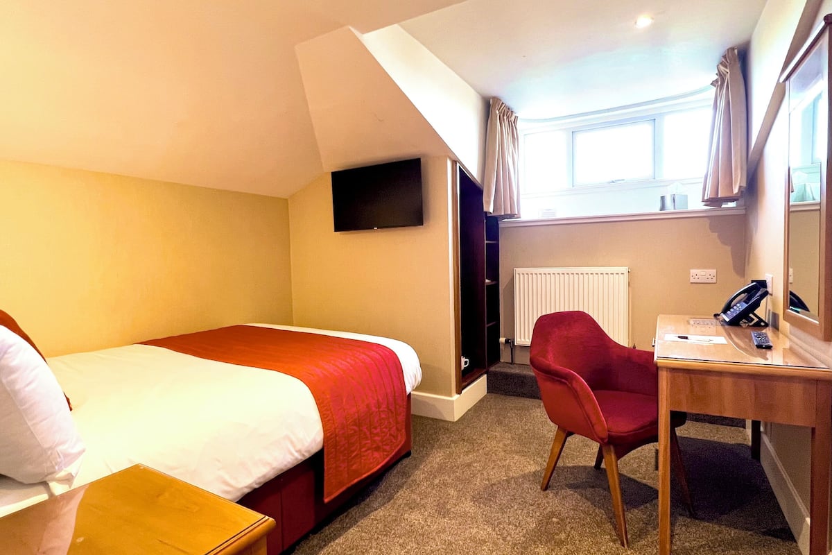 A hotel room with a bed, a desk, a chair, a TV, and a window with curtains.