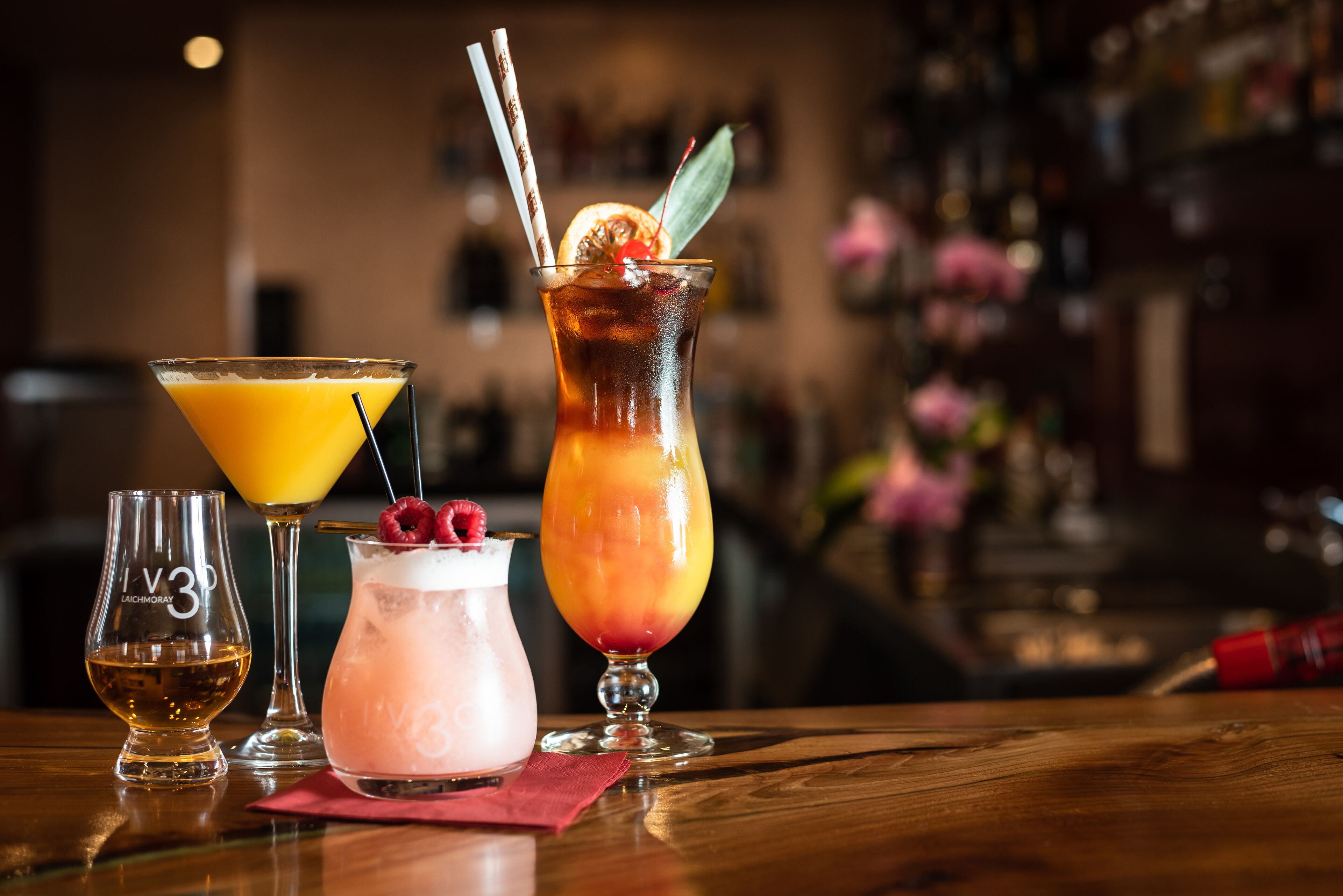 A bar setting with three drinks in different glasses, a small bottle, and a red napkin on the table.