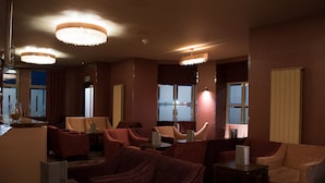 Un vestíbulo de hotel con varias zonas de estar, incluyendo sofás y sillones, dispuestas alrededor de una mesa central. Amplias ventanas ofrecen luz natural y vistas al exterior.