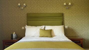 Un lit bien fait, avec une tête de lit verte, des oreillers blancs et verts, et une couverture jaune. Il y a deux tables de chevet, chacune avec une lampe, et une boîte de mouchoirs sur l'une d'elles.