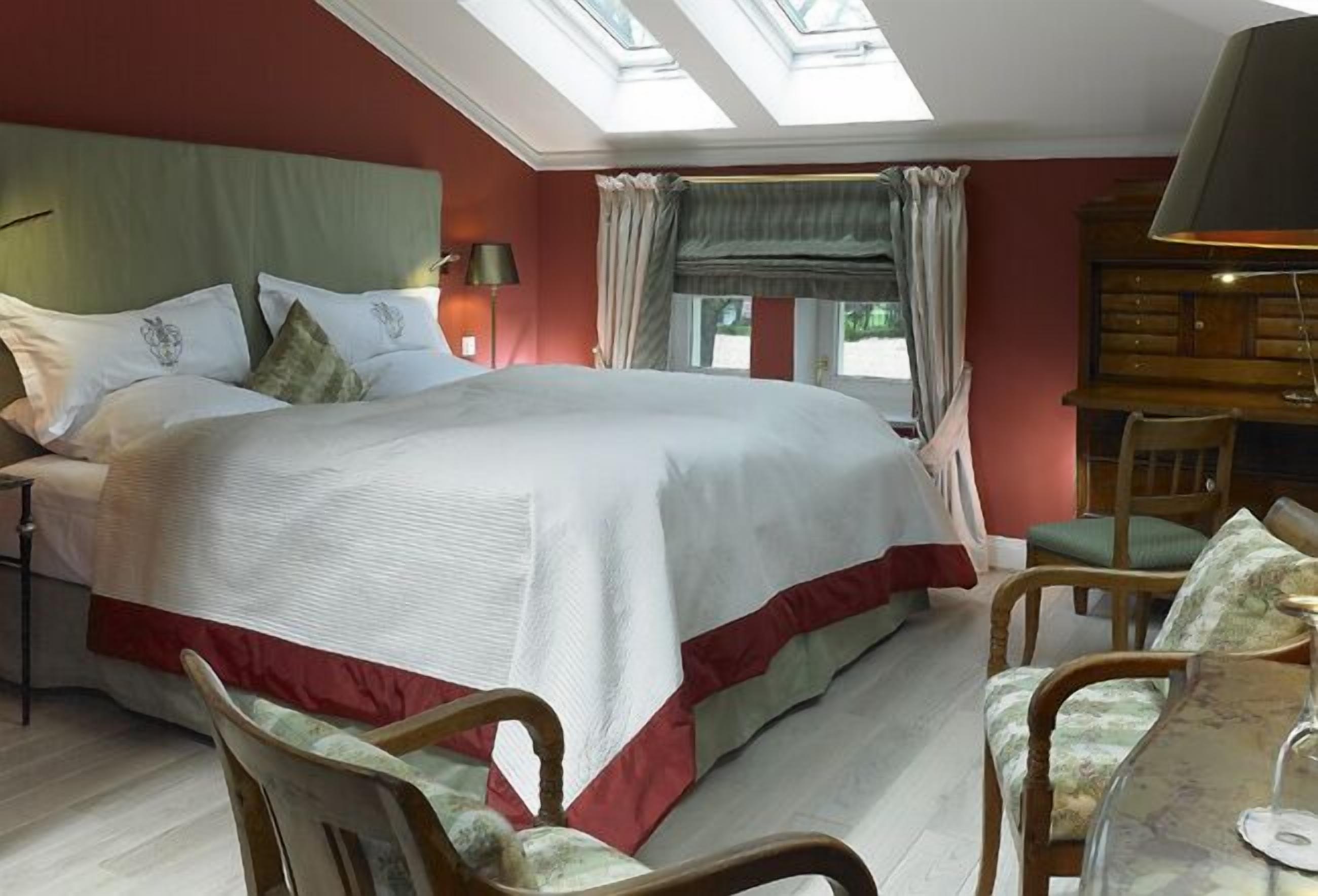 Une chambre avec un grand lit, une lucarne, un bureau avec une lampe et une chaise.