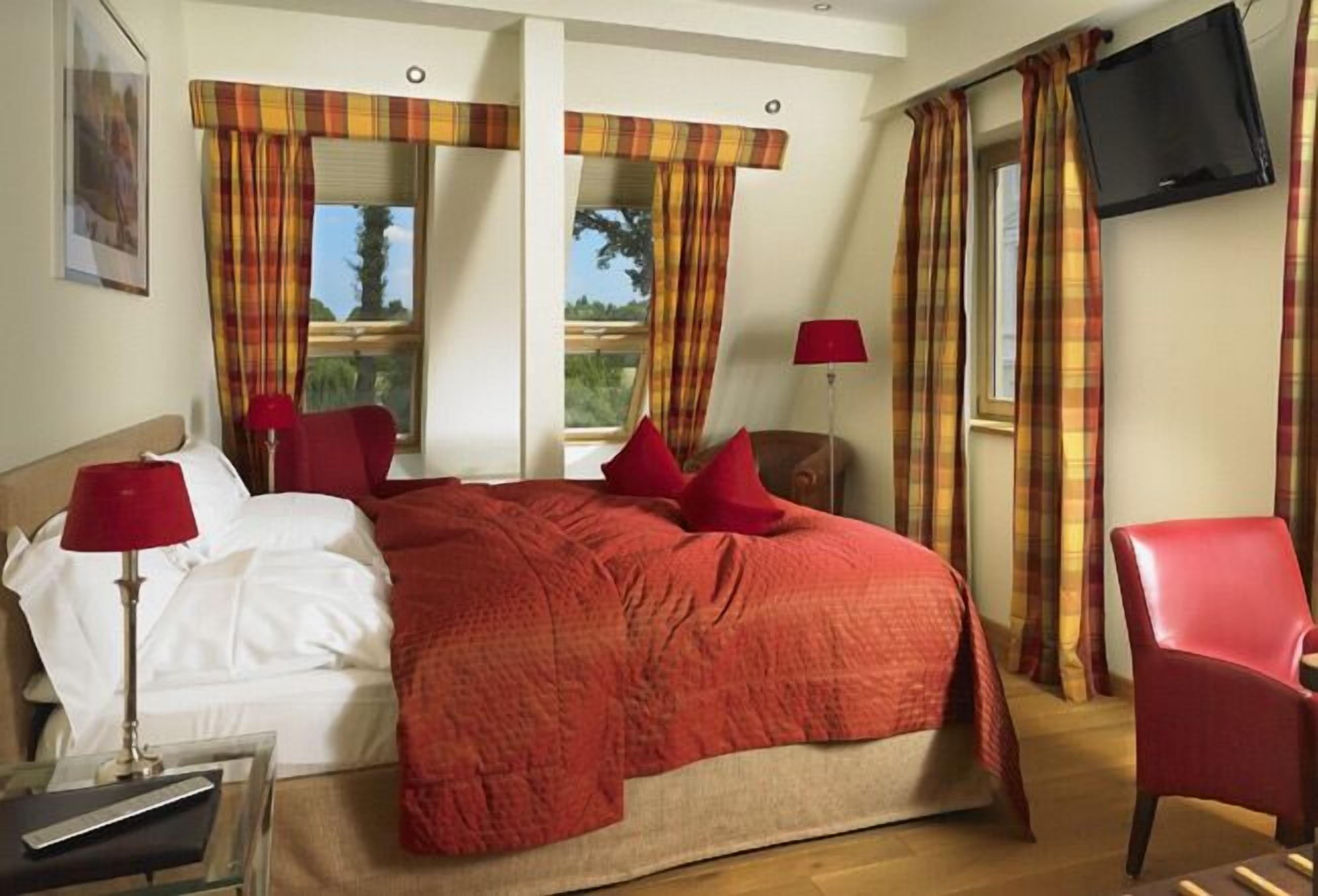 Un dormitorio con una cama grande, dos lámparas rojas, un televisor y cortinas de cuadros.