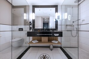 Features a sleek bathroom with a large mirror, toilet, sink, and shower area.