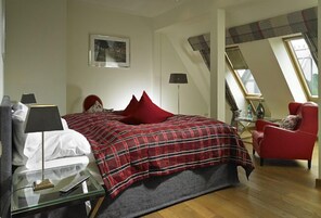 Un dormitorio con una cama, una silla roja, un escritorio con una lámpara y un cuadro en la pared.