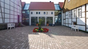 Une cour intérieure agrémentée d’un parterre central, de bancs et de bâtiments traditionnels à colombages.