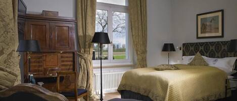 Une chambre à coucher avec un lit, un bureau et une chaise. Il y a une fenêtre avec des rideaux et un tableau au mur.