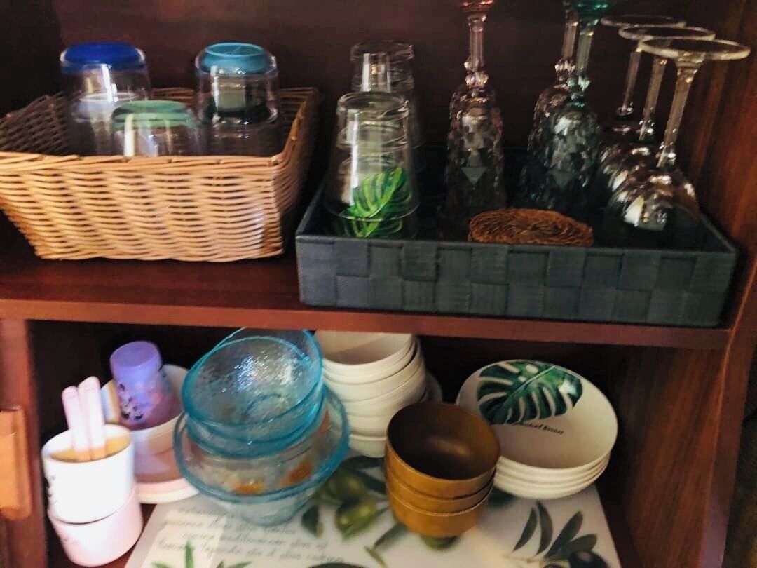 Una estantería con varios recipientes y objetos decorativos de vidrio, incluyendo frascos, botellas y una cesta.