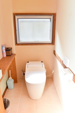 A compact bathroom with a toilet, a window above, and a small shelf with cleaning supplies. - Suite Terrace Ishigakijima (Ishigaki)