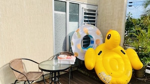 Una terraza de madera con una mesa de vidrio y una silla de mimbre, un pato inflable grande y un flotador con temática de piña.