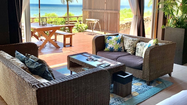 Una habitación con vistas al océano, que incluye mobiliario de mimbre, una mesa de madera y un banco.