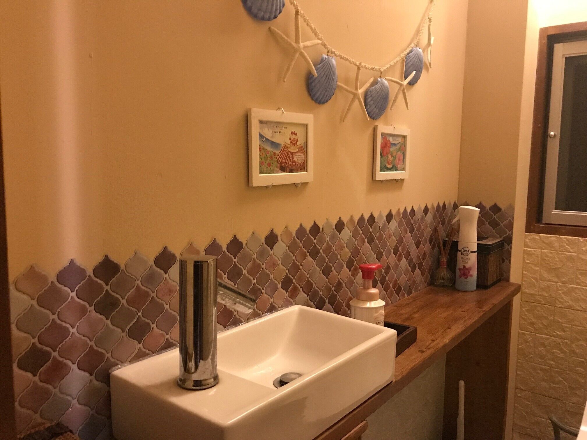 Un bagno con un lavandino bianco, un appendiabiti a stella marina decorativa e uno schienale piastrellato.