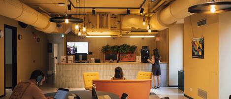 A modern interior with round tables, chairs, a reception desk, and a television screen displaying 'Friday Live Music'.