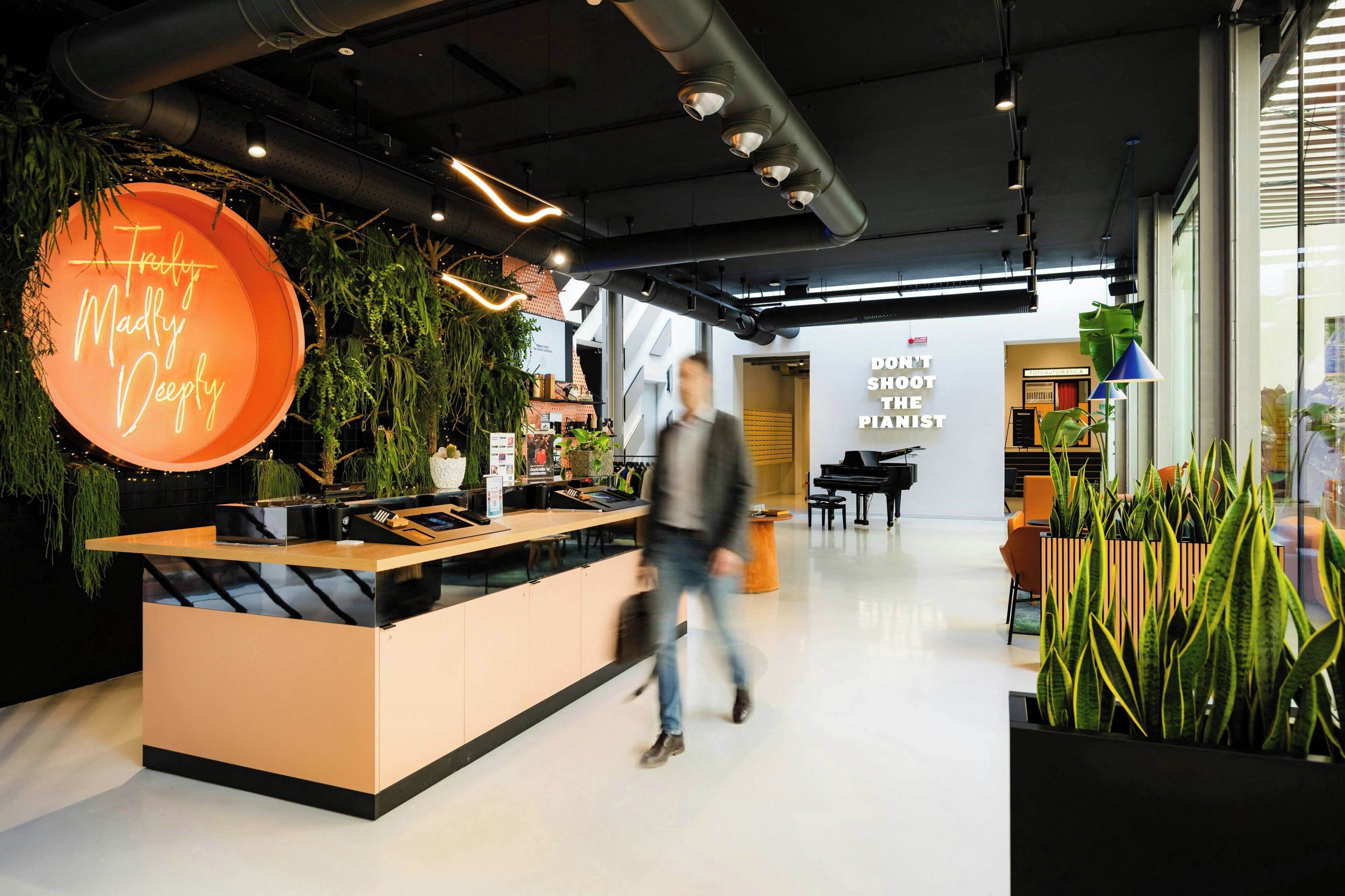 A modern reception area with a neon sign, a piano, and indoor plants.