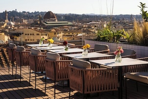 Outdoor seating with tables and wicker chairs, overlooking a cityscape with historic buildings.