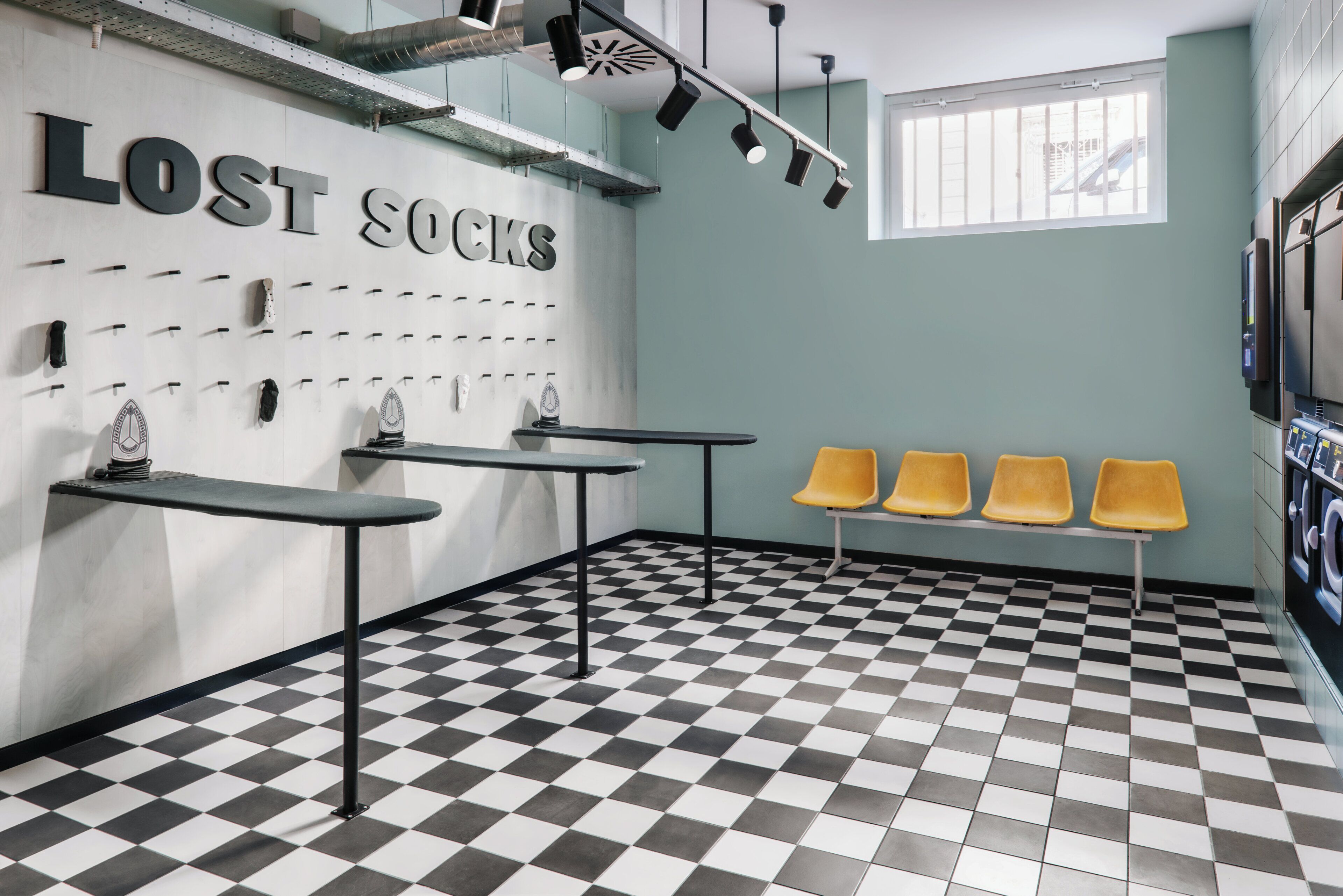 Une pièce avec un sol à carreaux, un mur sur lequel est affiché un panneau indiquant « CHAUSSETTES PERDUES », et trois chaises jaunes.