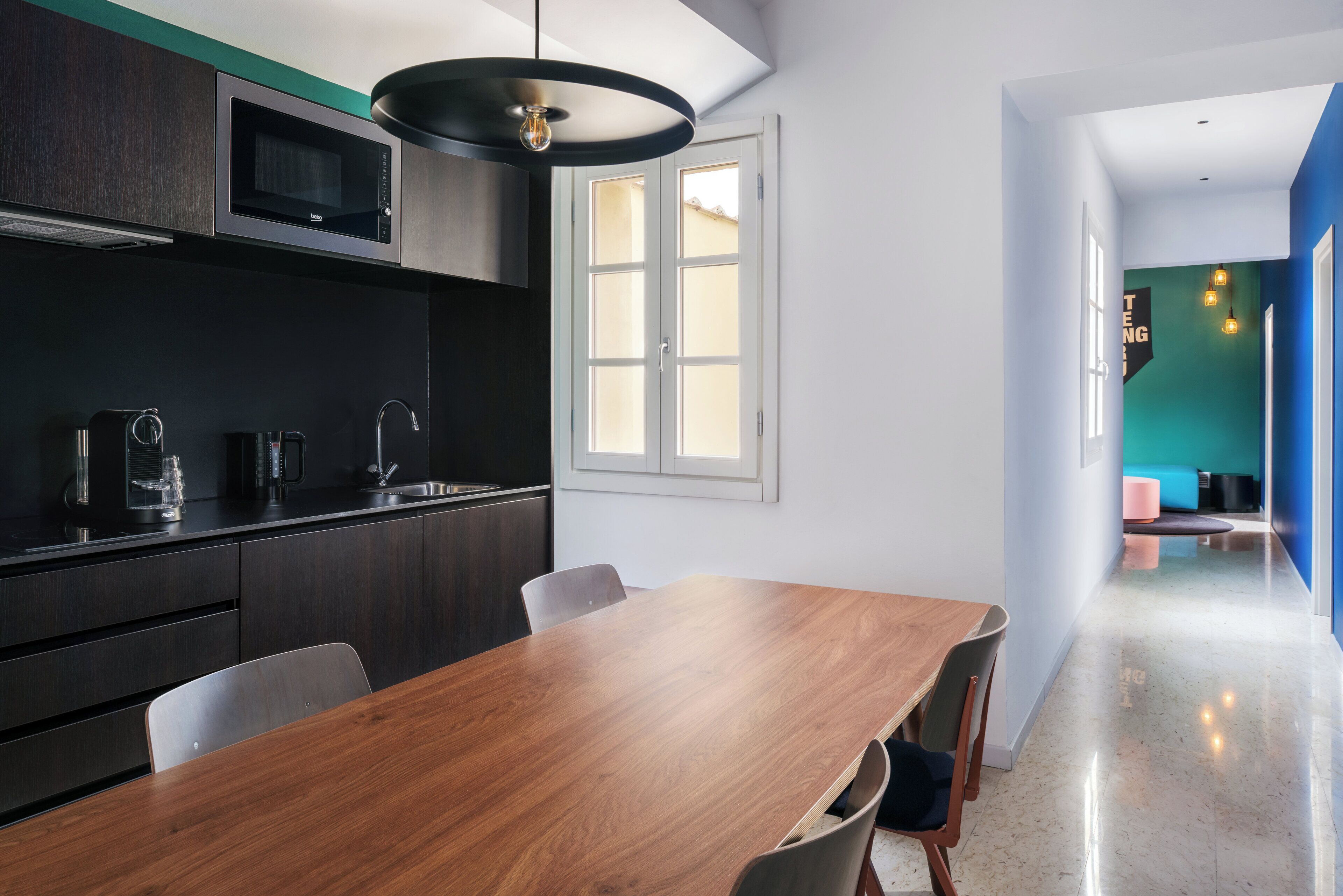 Une cuisine moderne avec des meubles de couleur sombre, une table à manger en bois et une vue sur l’espace de vie, accessible par une porte.