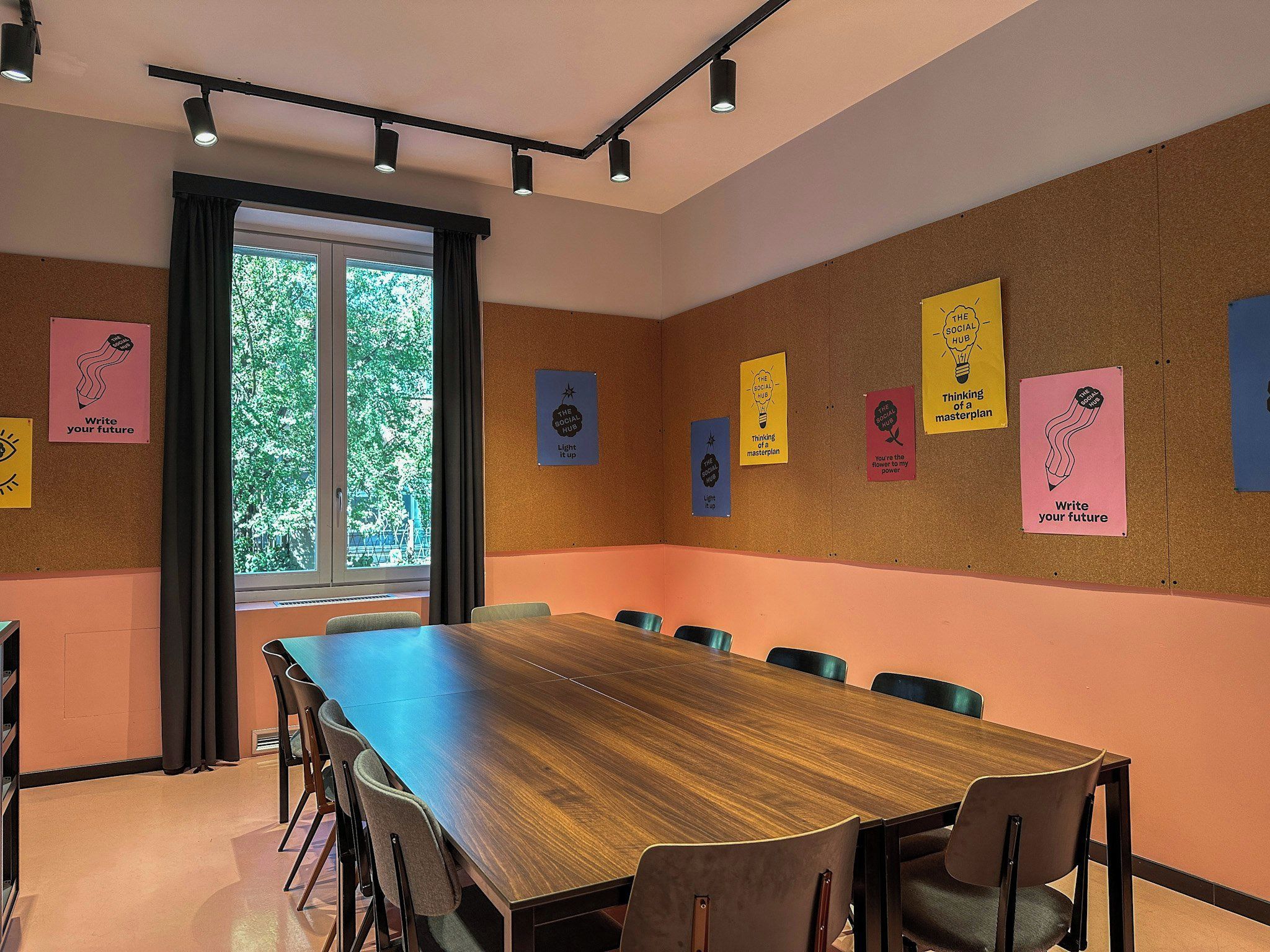 Un salón de conferencias con una larga mesa y sillas, una pizarra de corcho con carteles motivacionales y una ventana que da a vistas de árboles.