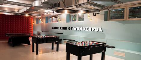 Una habitación con dos mesas de fútbol de mesa, un panel acústico rojo y una pared con el texto 'SOME KIND OF WONDERFUL'.